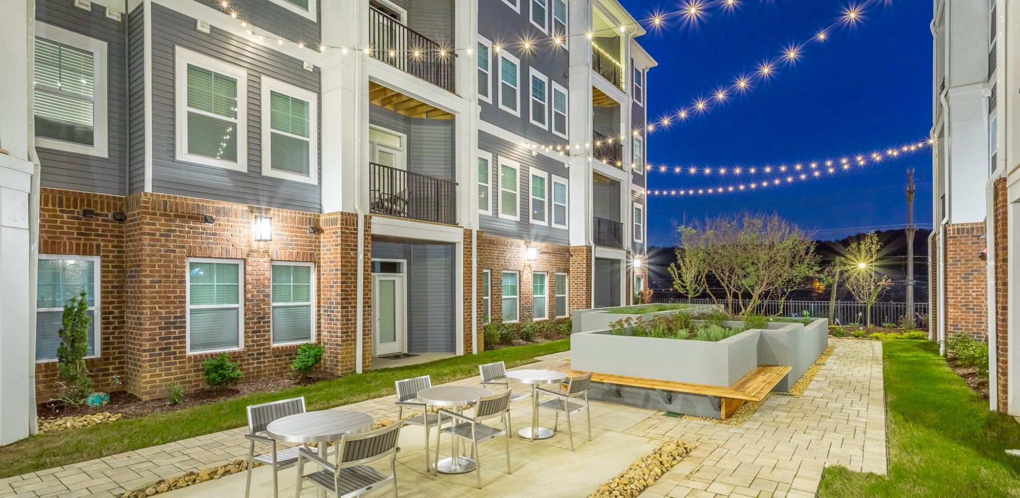 Hawthorne at the W apartments community exterior with courtyard seating, beautiful landscaping, and string lights